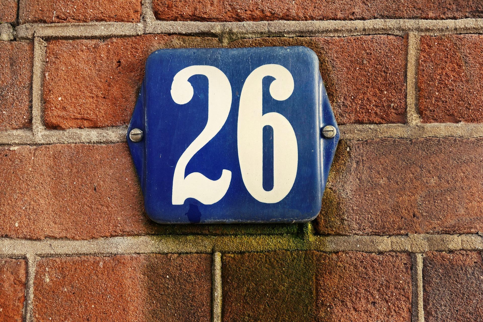 Blauw bordje met nummer 26 op een stukje muur.