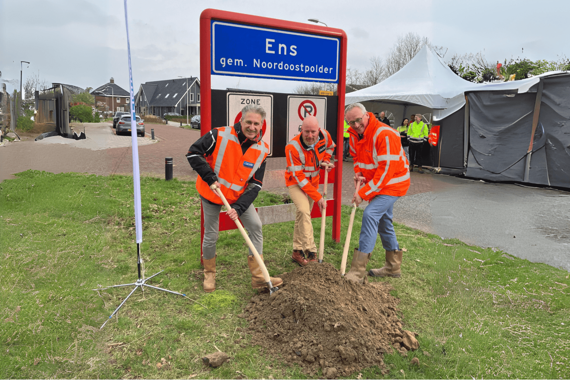 Wethouder van Amersfoort en 2 aannemers zetten een schep in de grond aan de Drietorensweg in Ens. Op de achtergrond het bord bij de ingang van Ens.